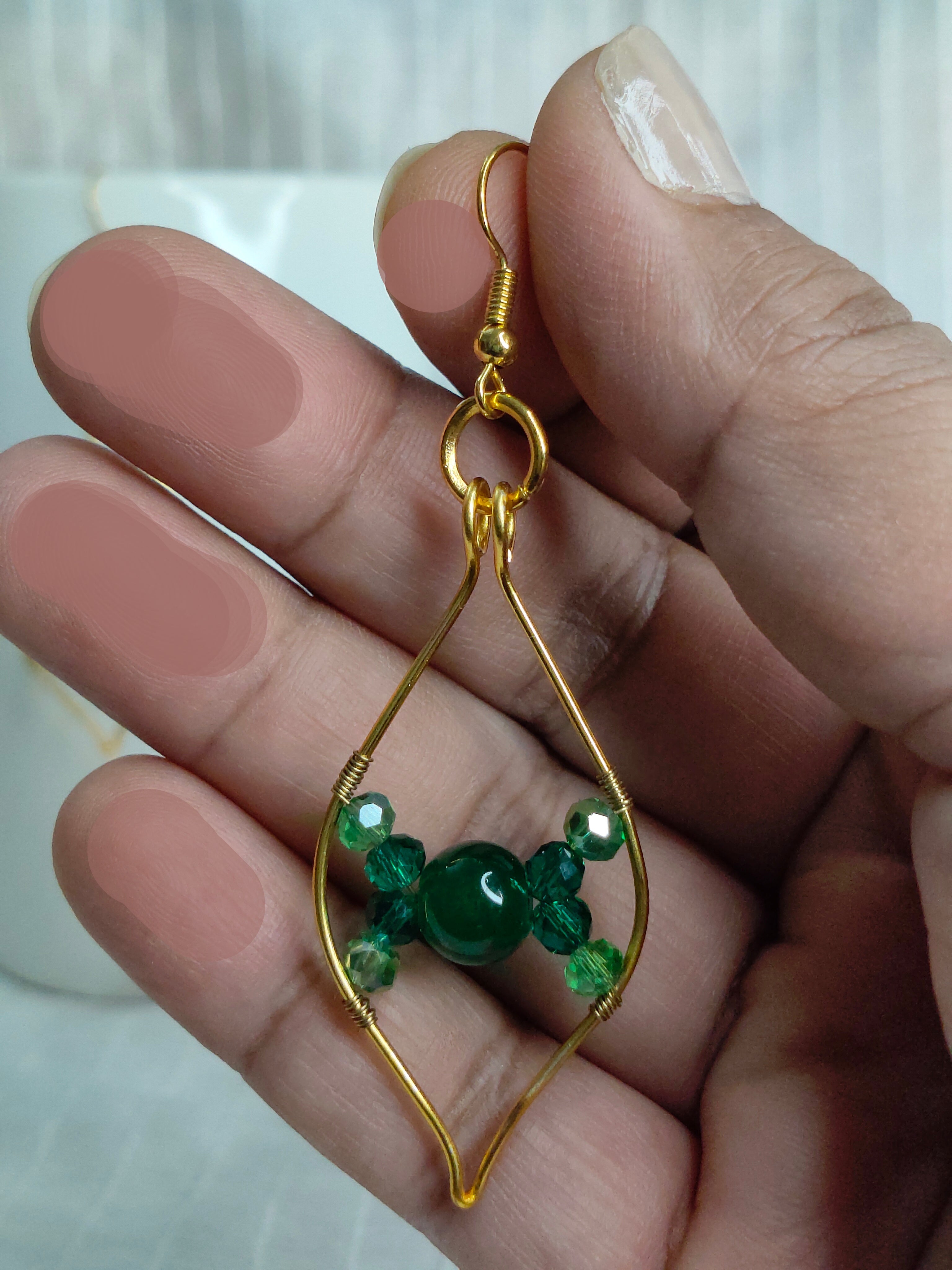 Gold earring with green beads held between fingers against a blurred background